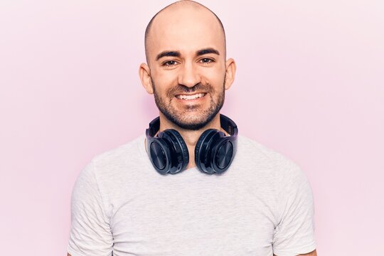 Young handsome bald man listening to music using headphones with a happy and cool smile on face. lucky person.