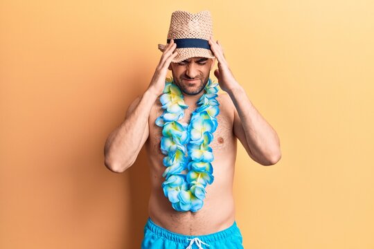 Young handsome bald man shirtless wearing swimwear and hawaiian lei with hand on head, headache because stress. suffering migraine.