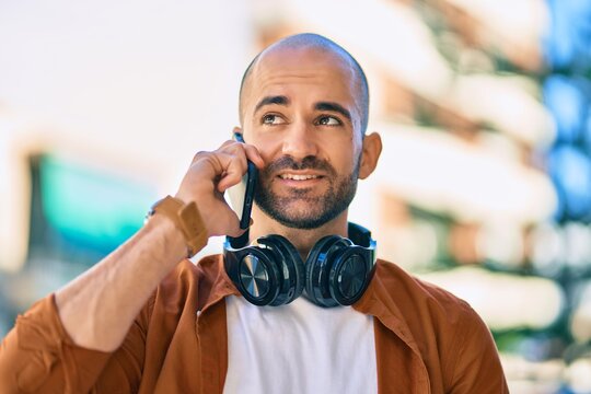 Young hispanic bald man smiling happy talking on the smartphone using headphones at the city.