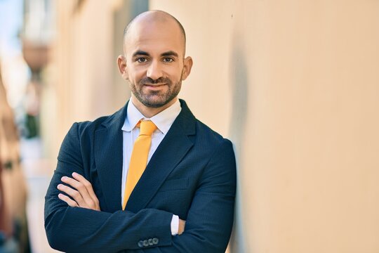Young hispanic bald businessman with arms crossed smiling happy at the city.