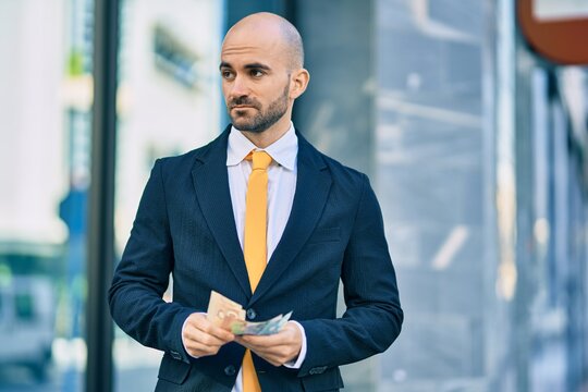 Young hispanic bald businessman with serious expression counting canadian dollars banknotes at the city.