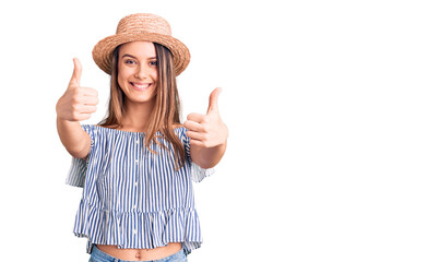 Obraz na płótnie Canvas Young beautiful girl wearing hat and t shirt approving doing positive gesture with hand, thumbs up smiling and happy for success. winner gesture.