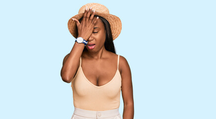 Young black woman wearing summer hat surprised with hand on head for mistake, remember error. forgot, bad memory concept.