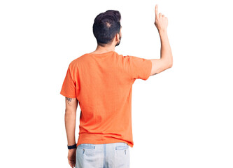 Young handsome man with beard wearing casual t-shirt posing backwards pointing ahead with finger hand