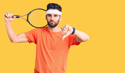 Young handsome man with beard playing tennis holding racket with angry face, negative sign showing...