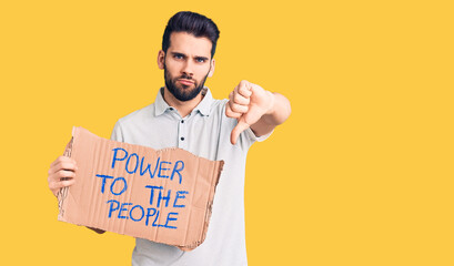 Young handsome man with beard holding power to the people cardboard banner with angry face,...