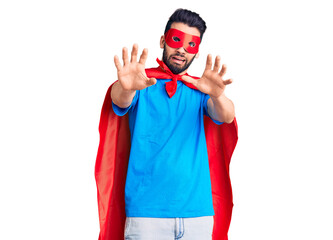 Young handsome man with beard wearing super hero costume afraid and terrified with fear expression stop gesture with hands, shouting in shock. panic concept.