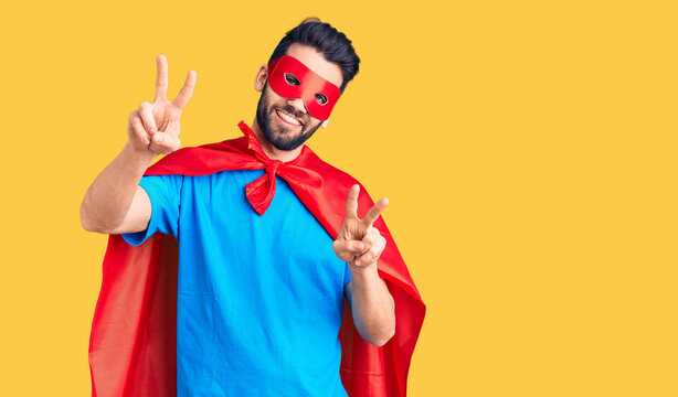 Young handsome man with beard wearing super hero costume smiling looking to the camera showing fingers doing victory sign. number two.