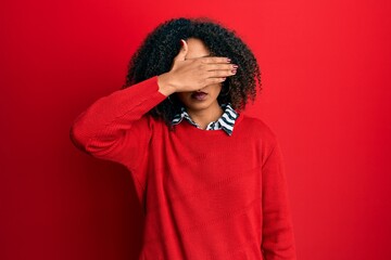 Fototapeta na wymiar Beautiful african american woman with afro hair wearing sweater and glasses covering eyes with hand, looking serious and sad. sightless, hiding and rejection concept
