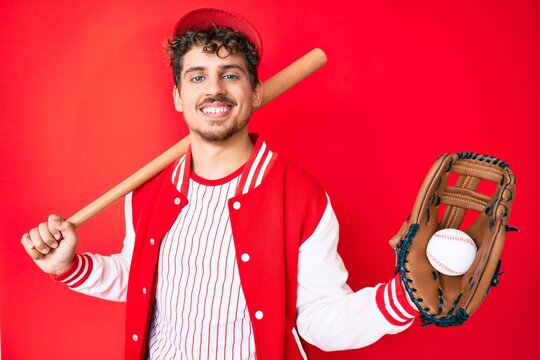 Young caucasian man with curly hair wearing baseball uniform holding golve and bat smiling with a happy and cool smile on face. showing teeth.