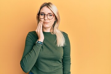 Young caucasian woman wearing casual clothes and glasses touching mouth with hand with painful expression because of toothache or dental illness on teeth. dentist
