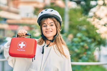 Caucasian sporty teenager girl wearing bike helmet holding first aid kit at the city.