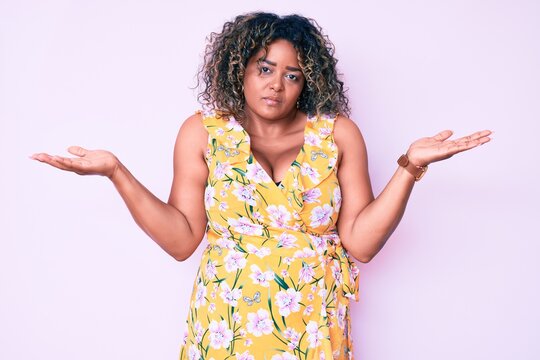 Young african american plus size woman wearing casual clothes clueless and confused expression with arms and hands raised. doubt concept.
