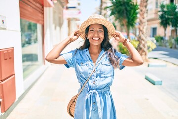 Young beautiful indian woman wearing summer hat smiling happy walking at the city.