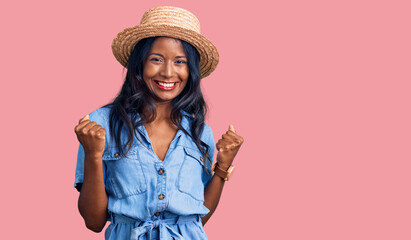 Young indian girl wearing summer hat very happy and excited doing winner gesture with arms raised, smiling and screaming for success. celebration concept.