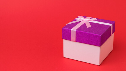 Gift box tied with a ribbon on a bright red background.