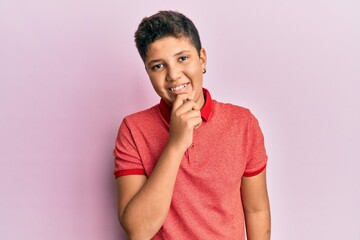 Fototapeta na wymiar Teenager hispanic boy wearing casual clothes smiling looking confident at the camera with crossed arms and hand on chin. thinking positive.