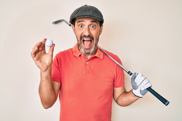 Middle age hispanic man holding golf club and ball celebrating crazy and amazed for success with open eyes screaming excited.