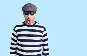 Middle age handsome man wearing burglar mask afraid and shocked with surprise expression, fear and excited face.