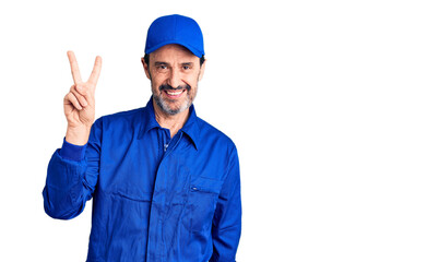 Middle age handsome man wearing mechanic uniform smiling looking to the camera showing fingers doing victory sign. number two.