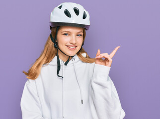 Beautiful young caucasian girl wearing bike helmet smiling happy pointing with hand and finger to the side