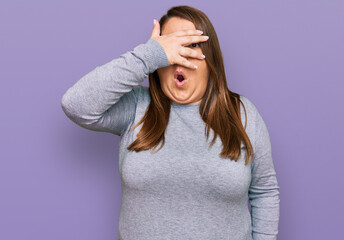 Beautiful brunette plus size woman wearing casual clothes peeking in shock covering face and eyes with hand, looking through fingers with embarrassed expression.