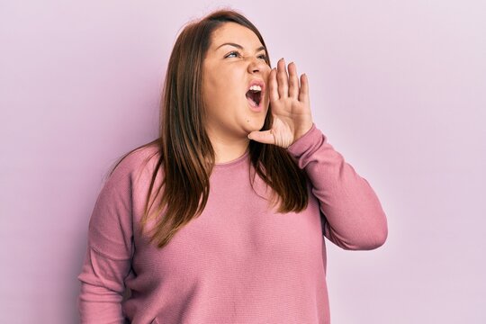 Beautiful brunette plus size woman wearing casual winter sweater shouting and screaming loud to side with hand on mouth. communication concept.