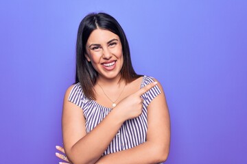 Obraz premium Young beautiful brunette woman wearing casual striped t-shirt standing over purple background smiling cheerful pointing with hand and finger up to the side