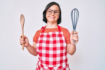 Brunette woman with down syndrome cooking using baker whisk and spoon smiling with a happy and cool...