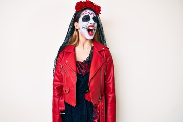 Woman wearing day of the dead costume over white angry and mad screaming frustrated and furious, shouting with anger. rage and aggressive concept.
