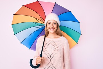 Young brunette woman under colorful umbrella looking positive and happy standing and smiling with a confident smile showing teeth