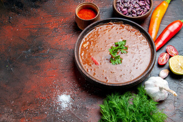 Tomato soup in a brown bowl and different spices garlic lemon on mixed color background