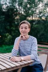 A young woman with short hair is waiting for her meal in a summer cafe in a park