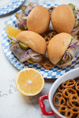 German fish sandwiches with white buns, herring fillet, red onion and pickles, vertical shot on a white concrete surface, close-up