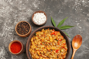 top view roasted eggplant salad in bowl different spices in bowls wooden spoon leaf on dark background