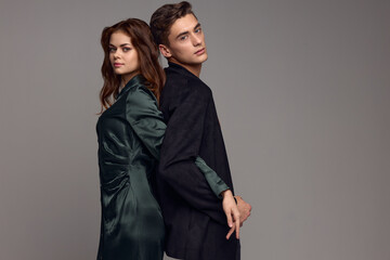 A sexy woman in a dress and a man in a suit stand with their backs to each other on a gray background