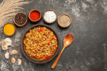 top view roasted eggplant salad in bowl different spices in bowls garlic wooden spoon on dark background free space