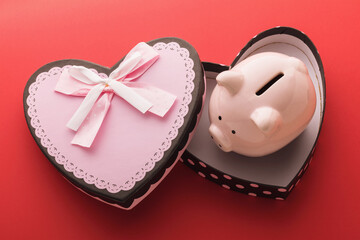 Piggy bank in an empty gift box on a red background. Concept on the topic of saving money for the holidays