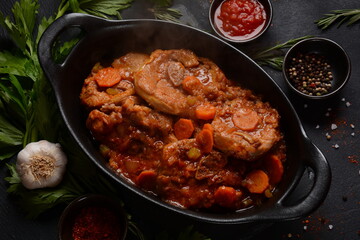 Ossobuco meat stew on the bone and vegetable sauce with carrots, tomatoes and celery in iron pan. Italian cuisine