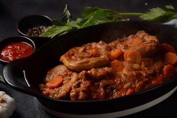 Ossobuco meat stew on the bone and vegetable sauce with carrots, tomatoes and celery in iron pan. Italian cuisine