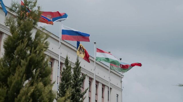 Flags of Russia, Hungary, Serbia, Belarus, Moldova, Azerbaijan, Armenia are waving on a flagpole in the city near administrative building in summer