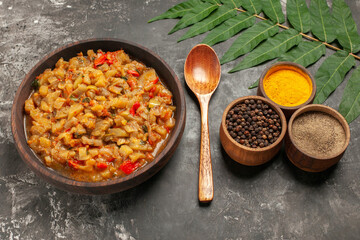bottom view roasted eggplant salad in bowl wooden spoon different spices in small bowls on dark background