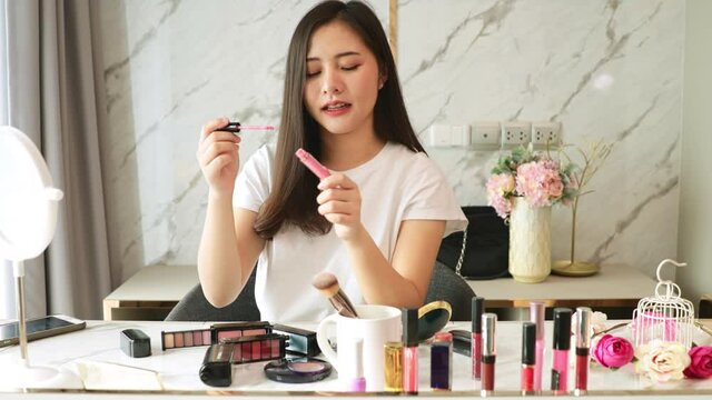 Portrait of young asian woman review cosmetics prosduct fan following channel, recording video make up lipstic cosmetic at home. Beauty blogger present beauty cosmetics.