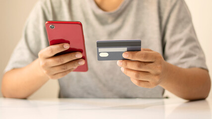 Asian man paying by credit card online while ordering on the internet at home, transaction idea using mobile banking application.