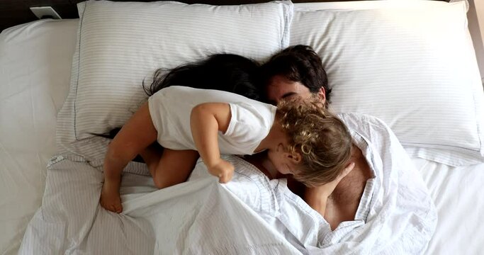 Cute family moment. Infant entering couple bed in the morning. Baby intruding in father and wife cuddle moment