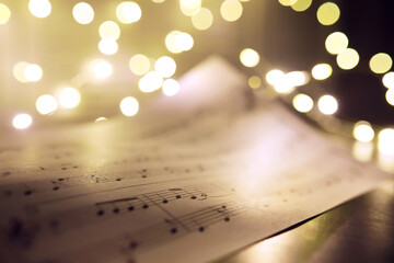 Old sheet with Christmas music notes as background against blurred lights. Christmas music concept