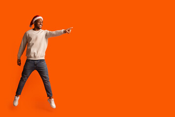 Christmas Promo. Excited Black Lady In Santa Hat Jumping And Pointing Aside