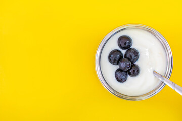 Natural flavor white yogurt in stainless steel cups and stainless steel spoons. Topping with grapes Fruits with a sweet and sour taste..Yellow background