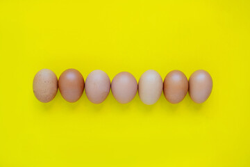 Brown fresh eggs side by side on a yellow background