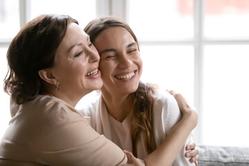Fototapeta premium Close up affectionate happy mature mother and daughter hugging, support and care, excited older mum and grownup child enjoying tender moment together, cuddling, sitting on cozy couch at home